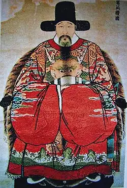 An elderly man sitting in an armchair, dressed in a luxurious robe with the characteristic wide Chinese sleeves, wearing an official’s hat on his head.