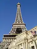 Ground-level view of a steel tower; the tower is broad at its base, rising from four separate legs. It then tapers, with each leg meeting to form a single, latticework column. Three platforms are visible at various heights up the side of the structure.
