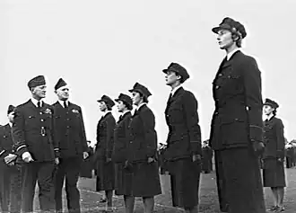 Three men and six women in dark-coloured military uniforms, outdoors