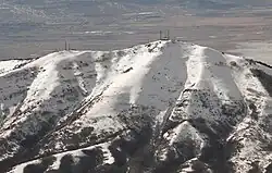 A snowcapped mountain with two clusters of communications towers at its peak