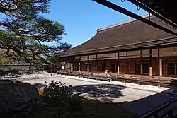 A wooden building with roofed veranda next to a raked gravel garden.