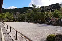 Shrubs cut in round shapes beyond raked gravel and large stones.
