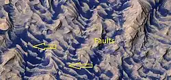 Close, color view of layers and dark dust on floor, as seen by HiRISE. Faults are indicated with arrows.