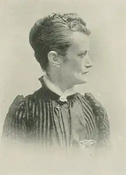 B&W portrait photo of a middle-aged woman wearing a dark, high-collared blouse with her hair in an up-do.