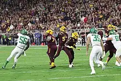 A centered photo of Daniels in an Arizona State Sun Devils uniform preparing to throw the football in a game against the Oregon Ducks