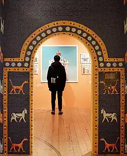 Visitor standing under a patterned archway looking at framed artwork on a peach-colored wall