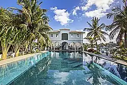 A two-story house sits at the end of a palm tree-lined pool