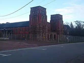 Large stone building with two towers behind a chain link fence