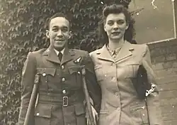 black and white photograph of a black man using crutches standing next to a white woman. Both people are wearing uniforms