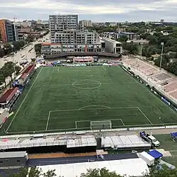 An aerial view of a soccer pitch with small grandstands on its right and bottom