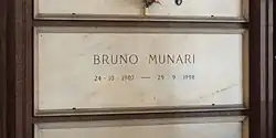 A white marble gravestone on the wall of a chapel, with only the name and dates of birth and death inscribed