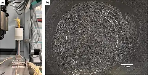 a) Scroll inside synchrotron X-ray beam at BAMline, BESSY 2. b) reconstructed cross-section of a scroll. Areas that contain metal appear bright, while the paper of the scroll is shown as light gray in color, and air in dark gray.[50]