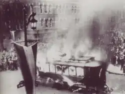 Photograph of a burning trolley car surrounded by a crowd