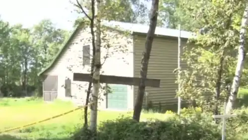 2-story cabin in a wooded clearing that is cordoned off with police tape.