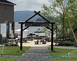 A sign for Camp of the Woods near a lake