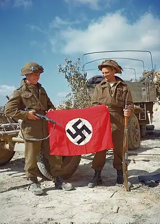 Canadian soldiers during Operation Overlord showing a captured Nazi flag as a war trophy outside Hautmesnil, France in August 1944. Photo: National Archives of Canada