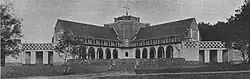 Two colonnaded wings branch diagonally each side from a squat central steeple