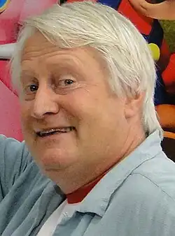 Closeup of a white-haired man smiling as he looks towards the camera.