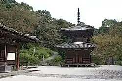 Small wooden two-storied pagoda shaped building with a square base and a round upper floor.