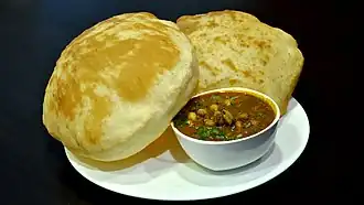 A bowl of chickpea curry on a plate with two large, puffy flatbreads.