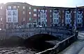 A view of a hump-back bridge with a set of commercial buildings on the opposite bank