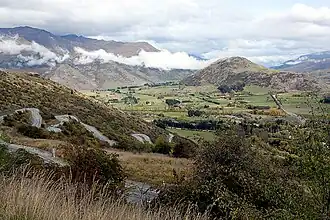 A view into a large valley with farmland from a hillside, with a windy road descending on the left