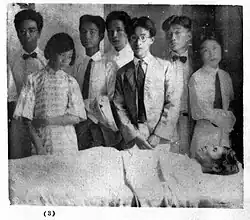 A black and white photo of a group of people around a man's deathbed