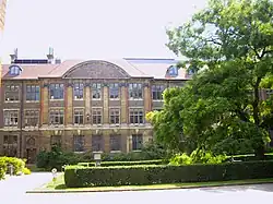 View of the Department of Plant Sciences, University of Cambridge, with a tree in full leaf obscuring the right side of the building, with lawns to the front of the building