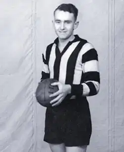 A dark-haired footballer in a long-sleeve black-and-white vertically striped guernsey and black shorts, holding a football