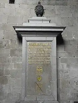Photographie d'une plaque tombale gravée fixée contre le mur par un socle maçonné