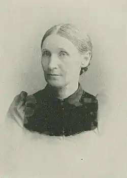 19th-century B&W portrait photo of a woman with her hair in an up-do, wearing a dark, fitted blouse.