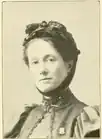 19th-century B&W portrait photo of a woman with her hair in an up-do, wearing a dark, fitted blouse.