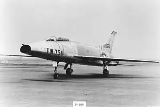 A jet aircraft with nose air intake sits on the tarmac, wearing U.S. Air Force insignia and "FW-754" coding on the nose