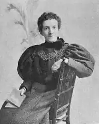 19th-century B&W portrait photo of a seated woman with her hair in an up-do, wearing a dark, fitted dress.