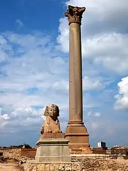 Tall Roman column known as Pompey's Pillar standing at the site of the Serapeum of Alexandria, with a stone sphinx in the foreground