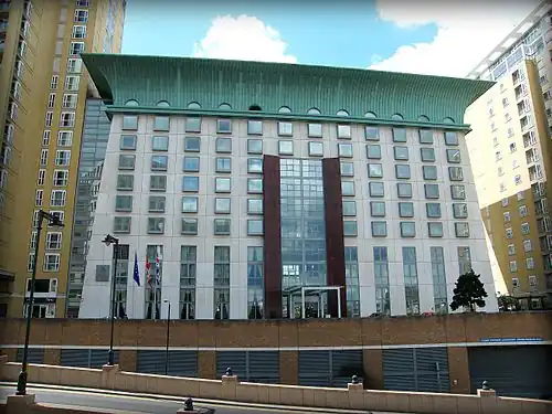 Modern hotel building with sloping walls and large green overhanging roof, designed in Egyptian Revival style