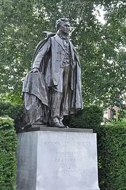 A color photograph of a bronze statue atop a gray, granite pedestal