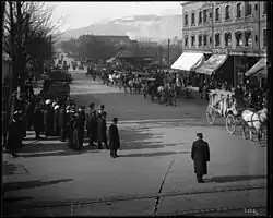 Black-and-white photograph of E. Pauline Johnson’s funeral procession moving along Georgia Street near Granville, with a horse-drawn hearse and carriages traveling past early 20th-century buildings as onlookers gather along the street.
