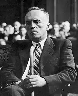 A black and white photograph of a suited old man seated at a trial