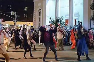 People dressed as various undead creatures dance in unison at night on a cordoned-off street