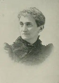 B&W portrait photo of a middle-aged woman wearing a dark, high-collared blouse with her hair in an up-do.