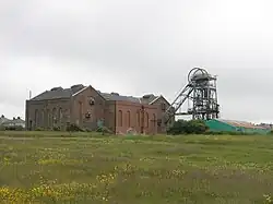 old brick mine building with a large steel hoist structure next to it, in a green field