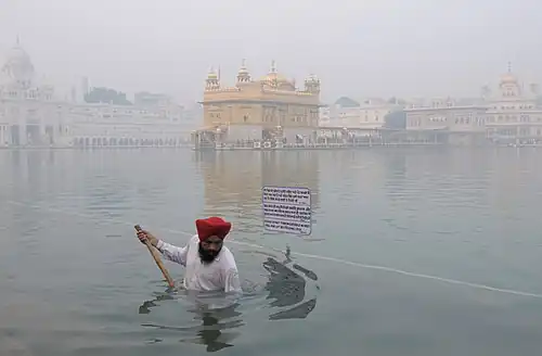 A Sikh pilgrim at the Golden Temple in Amritsar, Punjab, performing seva, or volunteer work, by helping clean the sacred pond