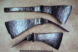 The top tool has a long pick with a verticla chisel-like edge, parallel to the broad axe head on the other end, the top of which is in line with the straight, untapering "pick", the bottome edge of which flares in the shape of a pendant equilateral triangle, save that the sharp edge is curved. The lower two tools have blades that are a bit closer to vertical, and narrower transverse azde heads, which are bent down so that they would form an angle of about 60 degrees to the missing wooden shafts.