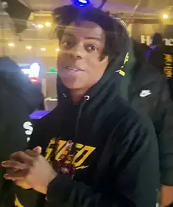 A young Black man looking at the camera smirking in a public place.