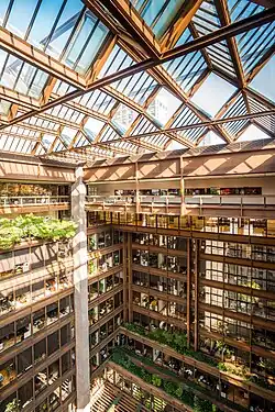 The interior atrium, with plantings inside, as seen from one of the upper floors. The roof, made of angled skylights, can be seen in the foreground. There are offices and windows across the atrium, in the background.