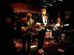 Three musicians standing in a row and performing on a dimly lit stage.