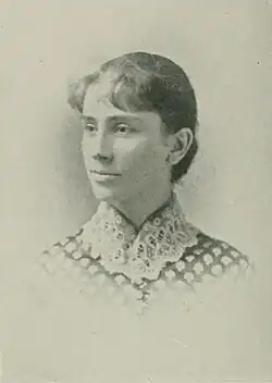 B&W portrait photo of a young woman with hair in an up-do, wearing a checkered blouse with a high-necked white lace collar.