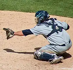 Jamie Burke, crouching in catchers gear, likely behind home plate, holding out his glove to receive a pitch
