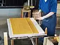 The papermaker carefully stacks each wet sheet of pulp left on the screen one by one.